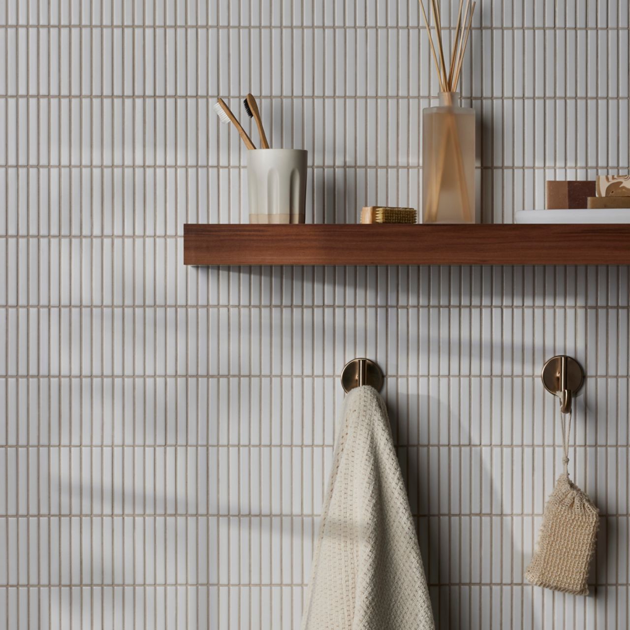 Bathroom wall tiled in long thin white tiles with a brown wood shelf holding toiletries