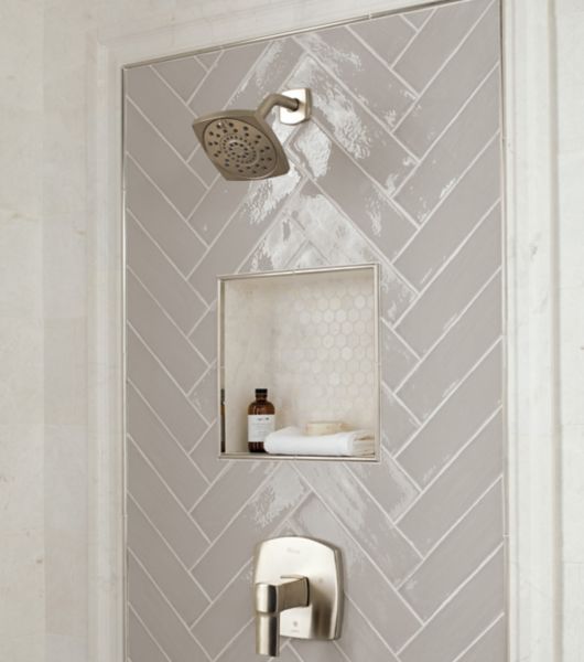 Shower wall with framed deco around shower fixtures and recessed niche in a herringbone pattern using linial subway tiles in taupe.  Frame is natural marble profile and stainless steel somerset.  Walls are also natural marble in a ivory color.