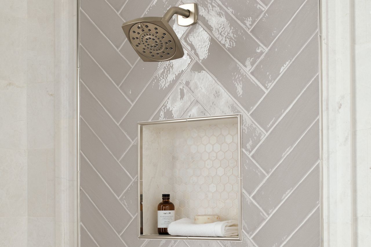 Shower wall with framed deco around shower fixtures and recessed niche in a herringbone pattern using linear subway tiles in taupe.  Frame is natural marble profile and stainless steel somerset.  Walls are also natural marble in a ivory color.