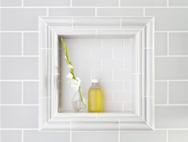 Subway tile on shower wall with recessed shelf framed by ceramic trim pieces.