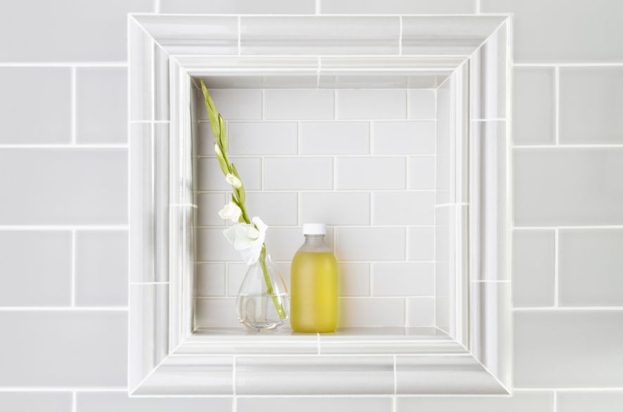 Subway tile on shower wall with recessed shelf framed by ceramic trim pieces.