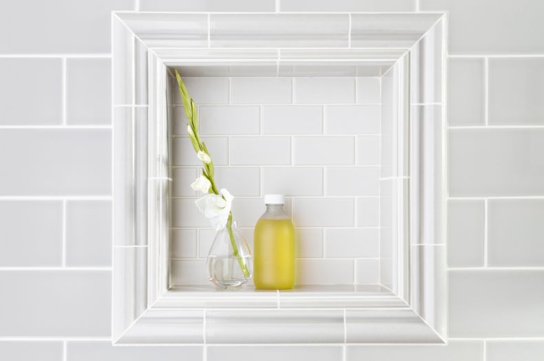 Subway tile on shower wall with recessed shelf framed by ceramic trim pieces.