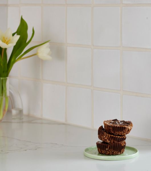 A kitchen backsplash featuring square white tile and light-colored grout.