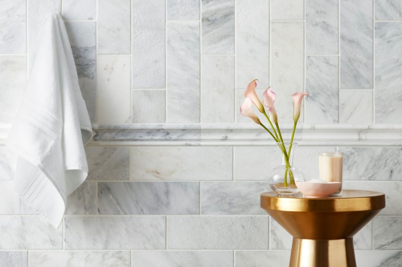 White and grey marble tiled shower wall with gold accent table.