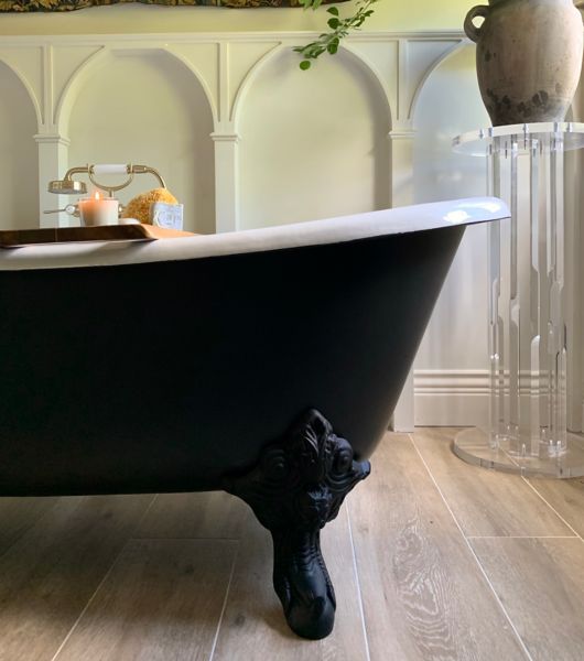 Black bathtub. White wall with arches and plant on a stand.