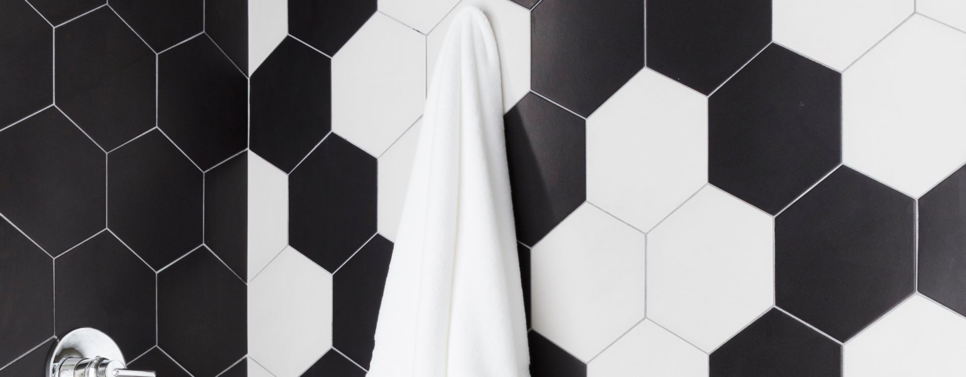 A shower with large black-and-white hexagon tile walls and small black-and-white hexagon floral patterned floor.