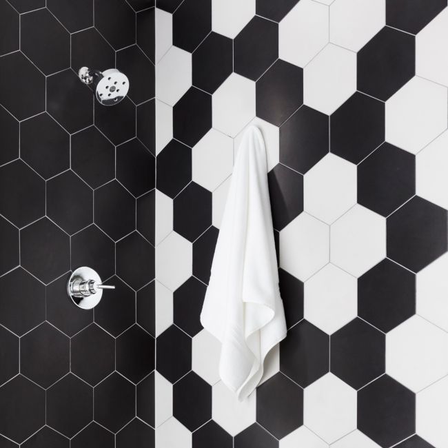 A shower with large black-and-white hexagon tile walls and small black-and-white hexagon floral patterned floor.