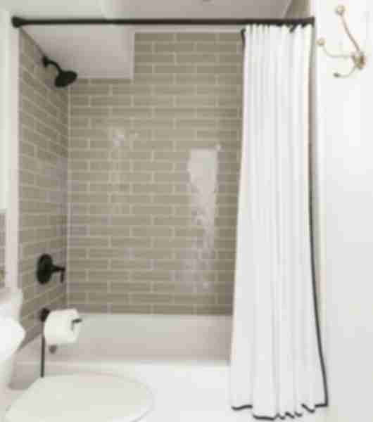 The interior walls of a tub/shower combination are covered with glass subway tile in a soothing neutral tone. Tiles are arranged in a brick layout and extend up to the ceiling of the shower.