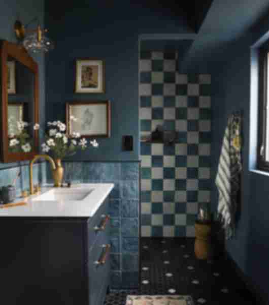 Bathroom with dark blue vanity and wall paint, and dark blue tiles on walls. Past the vanity is a walk-in shower with a floor-to-ceiling wall of dark blue and off-white tile arranged in a checkerboard pattern. The floor is covered in a mosaic of dark blue tiles with occasional small accents of white tile.