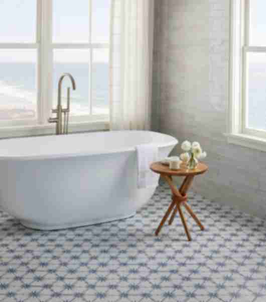 White tub in a bathroom with large windows. Small table with flowers and soap.