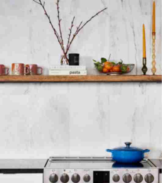 Open shelving on a white marble wall with a stove and blue pot.