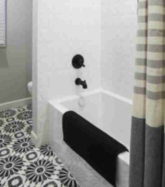 Black, white and grey bathroom featuring a white tub, dimensional white tile on the shower walls, and black and white floral patterned tile on the floors.