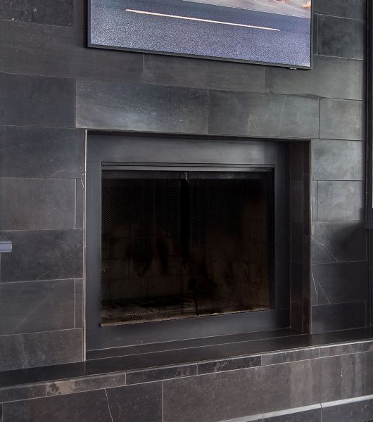 Large-scale rectangular tiles of black limestone cover a floor-to-ceiling fireplace wall. The tiles are laid horizontally and staggered to form a brick-lay pattern.