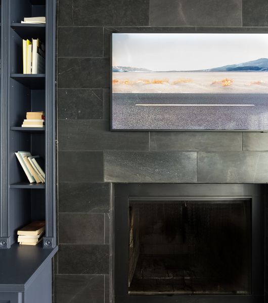 The wall around and above a black-framed fireplace is covered with dark and dramatic honed limestone tiles in an oversized subway shape, arranged in a brick layout.