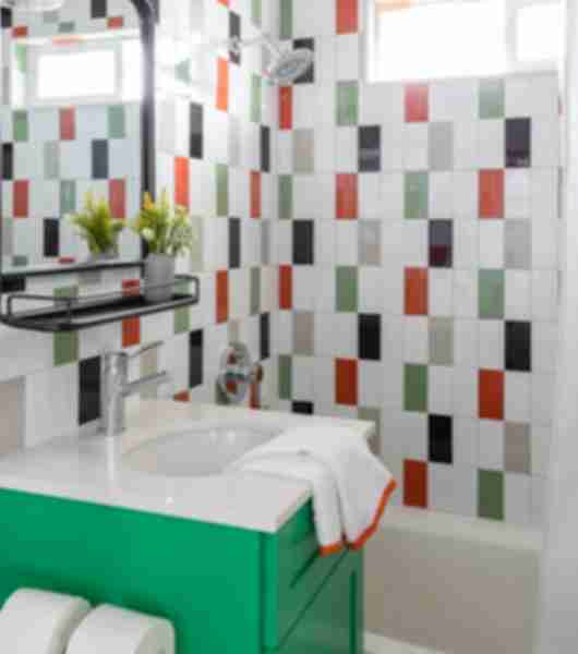 Green sink vanity before a shower with green, orange, black, tan and white tile.
