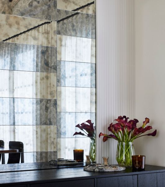 This dining room showcases oversized, rectangular mirrored tiles in shades of dark grey and gold. Each shade features an antique-effect patina that complements the main color of the tile. The tiles are arranged in staggered rows of alternating colors above a dark buffet cabinet.