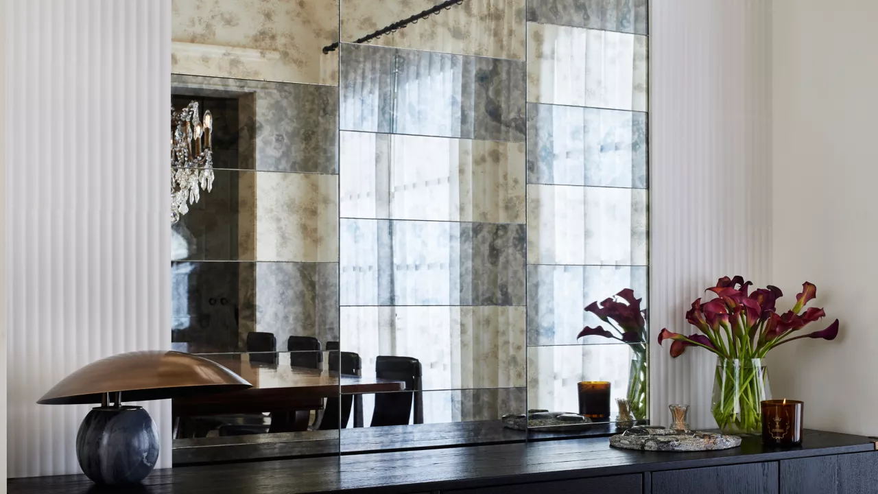 This dining room showcases oversized, rectangular mirrored tiles in shades of dark grey and gold. Each shade features an antique-effect patina that complements the main color of the tile. The tiles are arranged in staggered rows of alternating colors above a dark buffet cabinet.