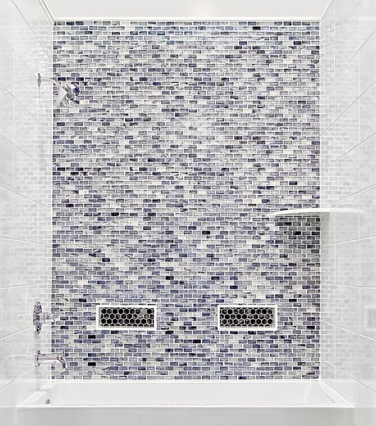 Tub surround in bathroom with tile glass brick mosaic feature wall, white ceramic tile side walls, niches on back wall with accent hex mosaic and a corner shelf for storage.