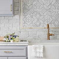 Thumbnail image of Backsplash tiled in kitchen area. Beveled marble subway tile with waterjet cut mosaic accent deco above sink and framed in marble and gold profiles. Counter top is also marble and matching profiles in whites and greys.