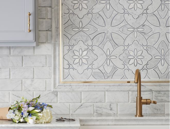 Kitchen backsplash with white marble mosaic in floral pattern and gold accents.