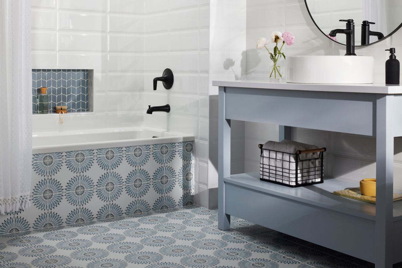 This whimsical bathroom features a blue geometric-floral patterned tile floor, white beveled subway tile walls and a leaf-shaped tile shower niche.