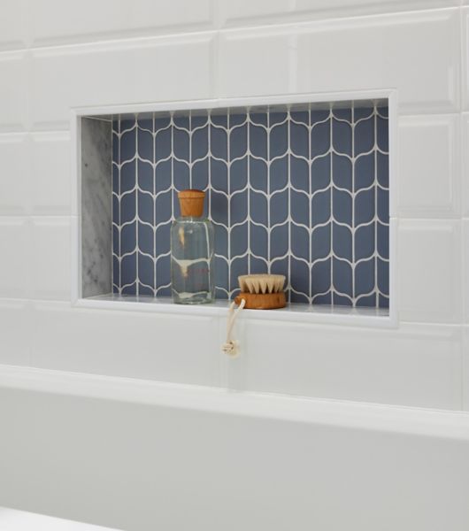 Blue leaf-shaped mosaic tile is used in a recessed shower niche. The blue tile stands out against the beveled white subway tile used on the majority of the tub/shower wall.