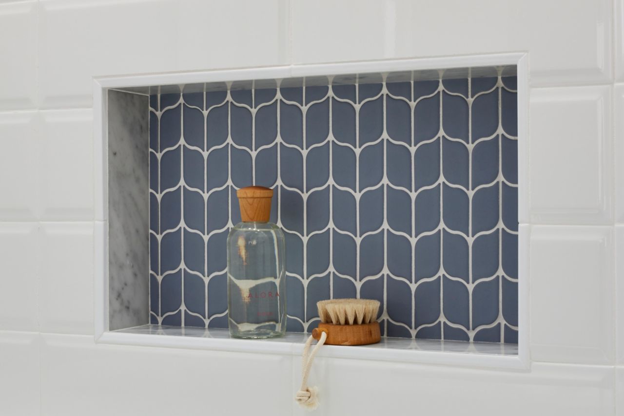 Blue leaf-shaped mosaic tile is used in a recessed shower niche. The blue tile stands out against the beveled white subway tile used on the majority of the tub/shower wall.
