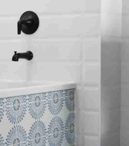 Detail of a bathtub area featuring beveled white subway tile on walls and patterned blue and white tile on the sides of the tub.