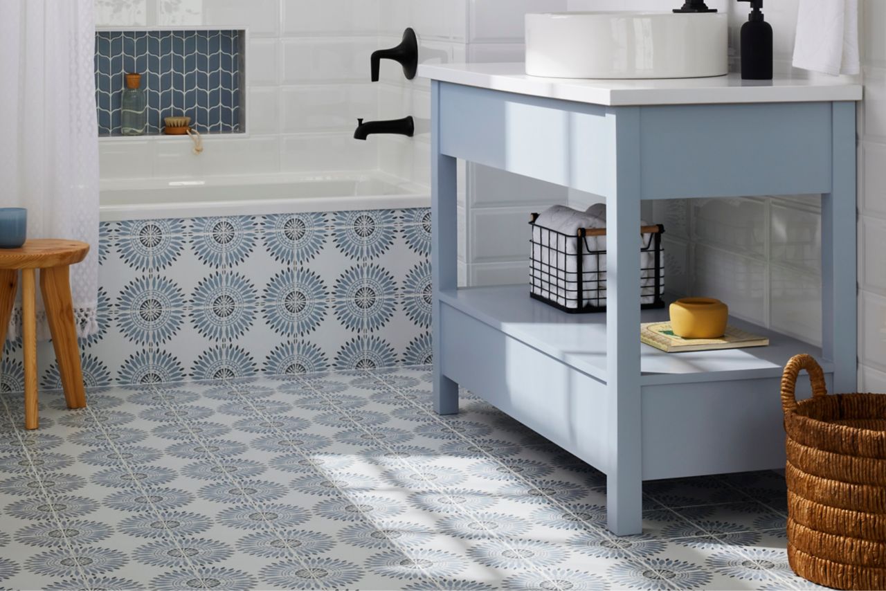 Blue bathroom with blue and charcoal geometric flower patterned floor extended up the side of the tub.