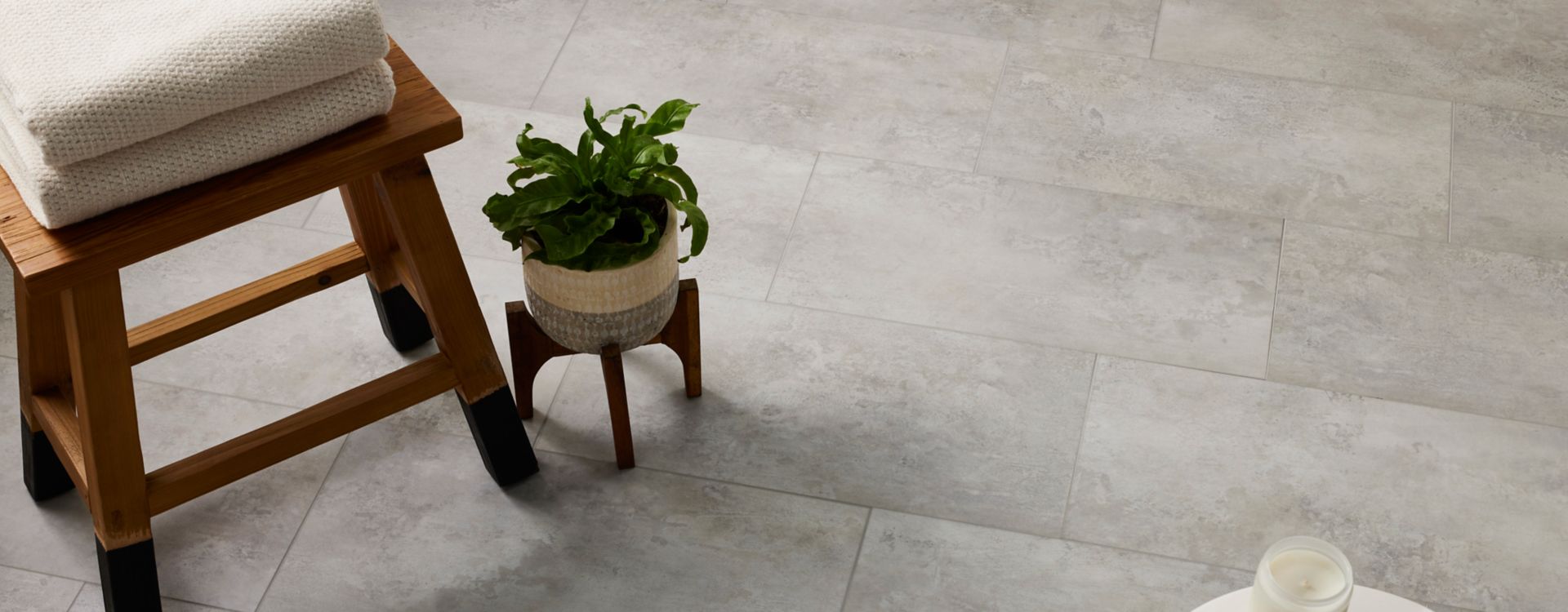A modern, minimalist bathroom features neutral grey-toned luxury vinyl flooring that looks like realistic natural stone.
