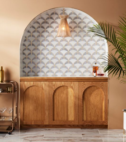 An elegant home bar backsplash features Art Deco-inspired waterjet marble mosaic tile in shades of white and grey marble, with gold accents.