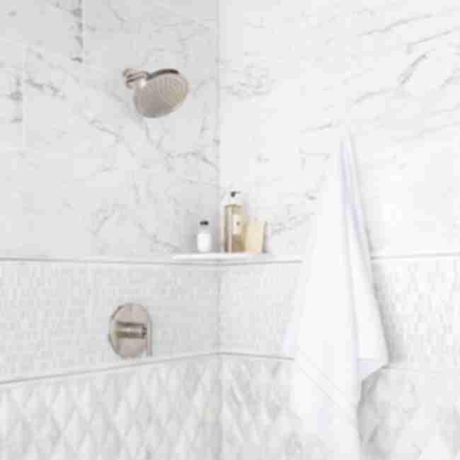 Shower walls tiled with porcelain marble look in a large format, natural marble tile and accessories including corner shelf.  Metal and natural marble profiles frame metal and glass multi finish mosaic accent.  Tile tones are balanced in neutral grey, taupe, white and ivory tones.