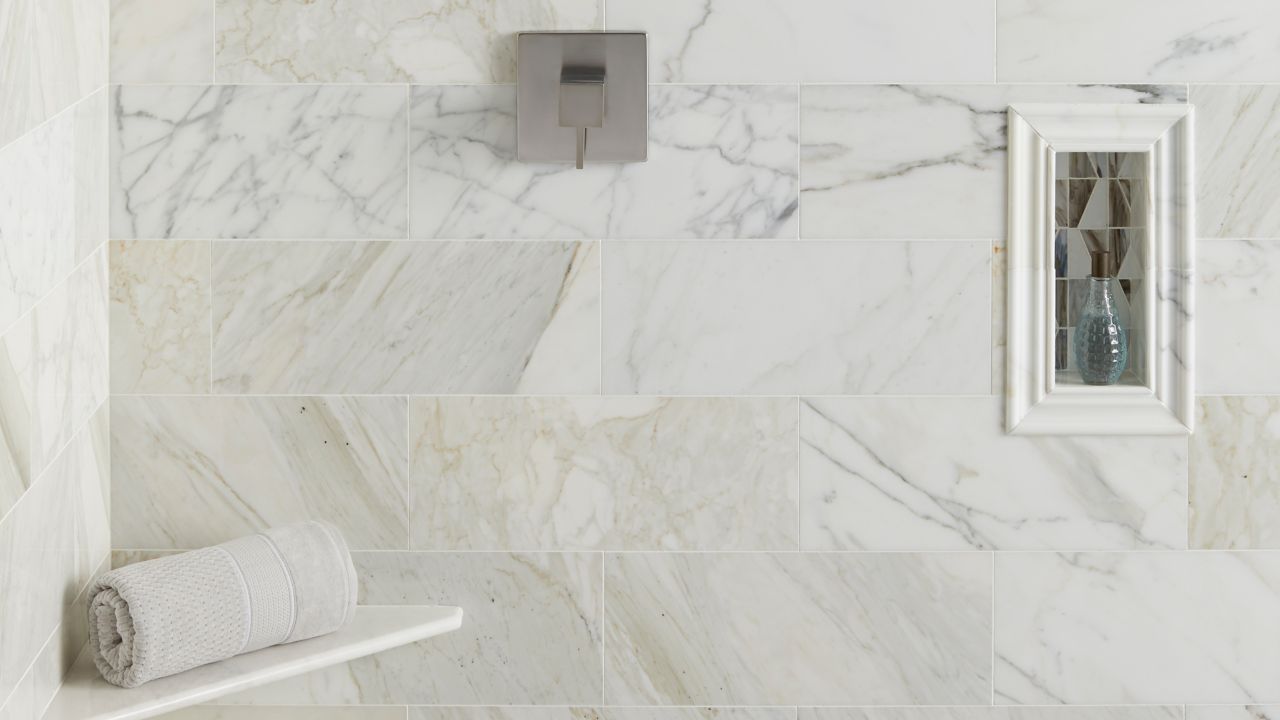 This marble tile has a polished finish and a cloudy white base with gold veining, profiles are the same marble and accent border is a glass geometric patterned mosaic tile.