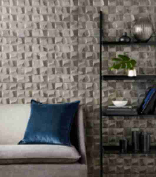 Accent wall of textured tile in light toned gold with shadowing behind a sofa and black metal book shelf.  
