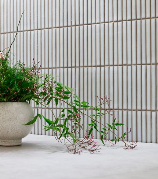 White mosaic handmade-look tile creates an artisanal charm. Above a shelf with a potted plant.