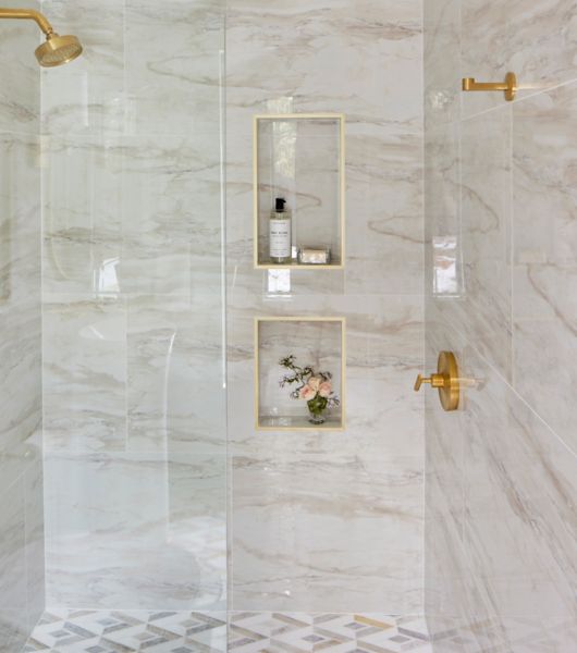 Shower with marble tile, gold fixtures and two small niches.