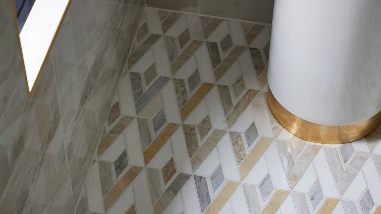 Corner shot of a shower with gold, white and grey diamond-shaped mosaic tile floor.