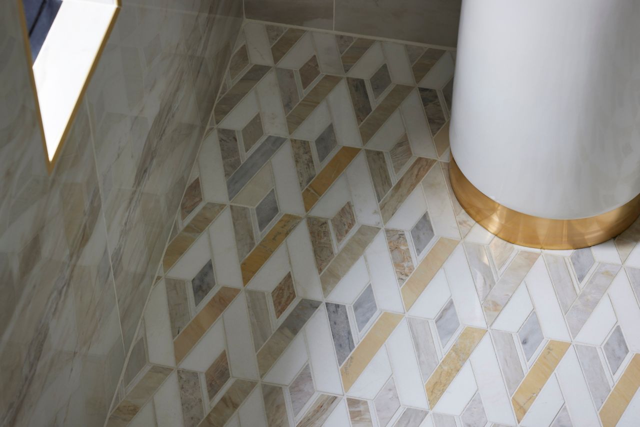 Corner shot of a shower with gold, white and grey diamond-shaped mosaic tile floor.