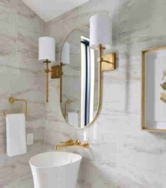 White sink with gold fixtures, gold-rimmed mirror, wall sconces and white and gold picture