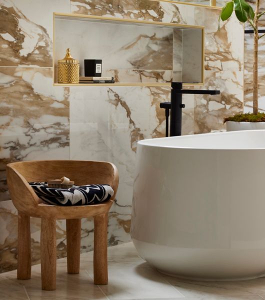 Bathroom with tub and small wooden chair. White tile with bold brown veining on the walls.