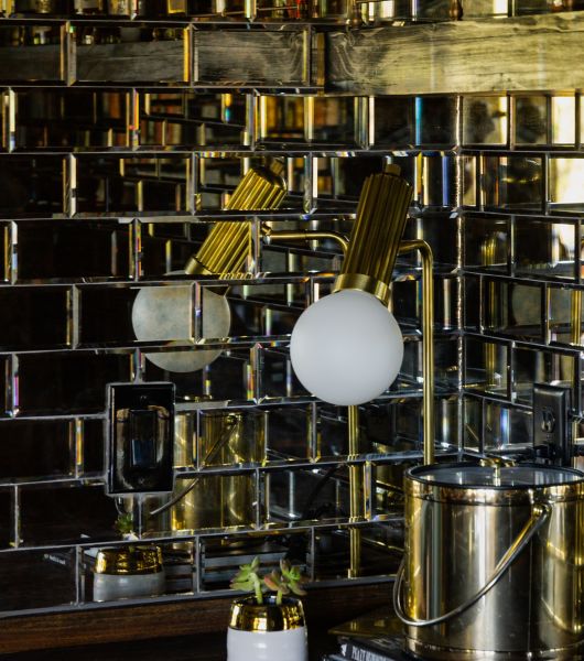 Reflective mirrored glass mosaic wall tile above a bar with a lamp and ice-bucket.