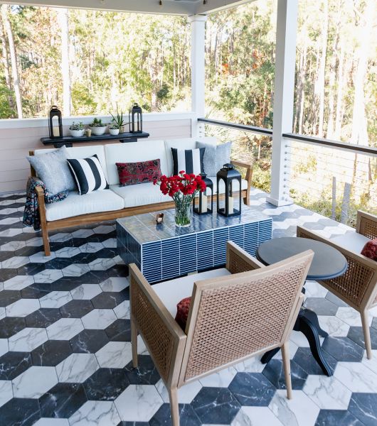 Black and white hexagon porcelain tiles create a zig-zag striped pattern on a three-season porch with couch, chairs and coffee table.