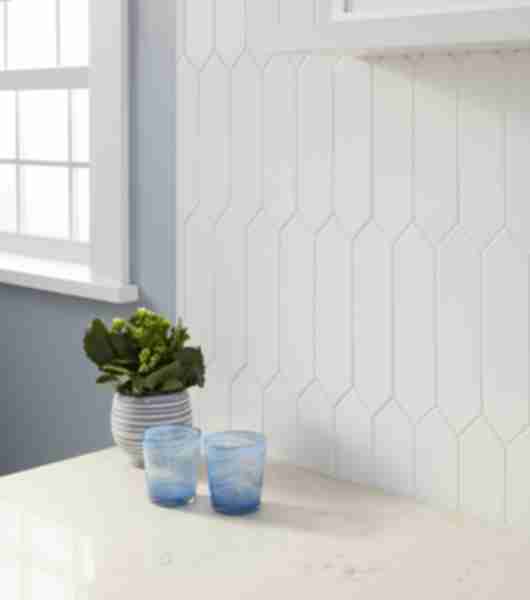 Kitchen backsplash with white picket shaped tile ran vertically above counter top.  Cabinets are white with black hardware.