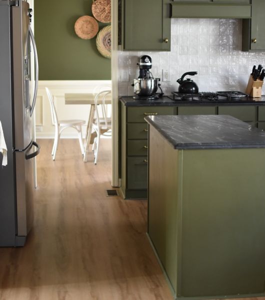 Green kitchen with brown, wood-look vinyl flooring