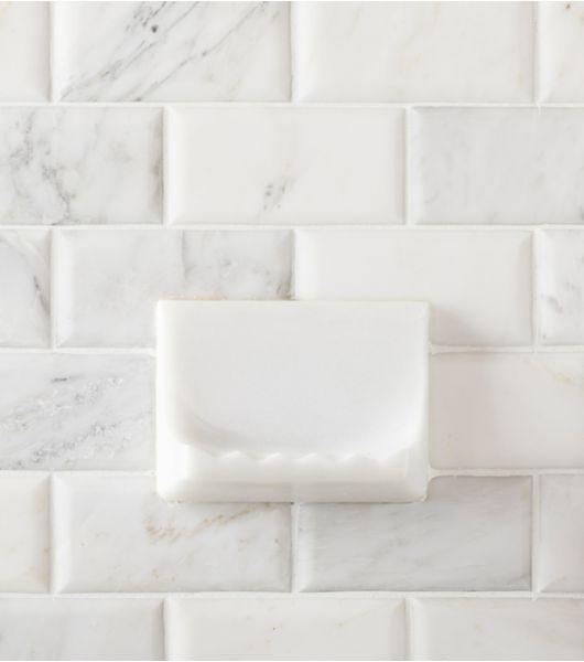 Shower wall with white marble subway tile and soap dish.