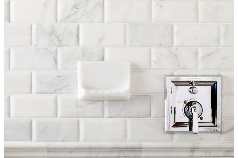 Shower wall with white marble subway tile and soap dish.