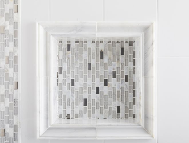 Shower wall with white marble, glass and metal mosaic accents, and recessed shelf. 