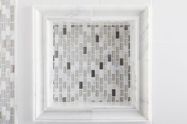 Shower wall with white marble, glass and metal mosaic accents, and recessed shelf. 