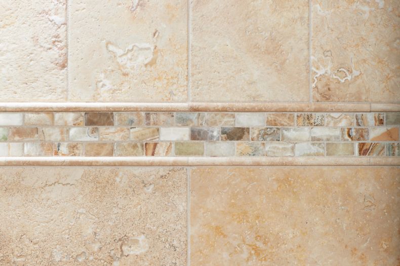 Shower wall with beige tile, mosaic accent, and soap dish.