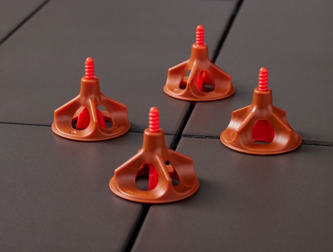 Four orange tile leveling caps on charcoal colored tiles. 